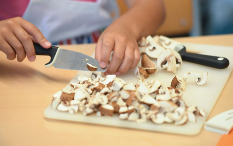 Eine Schülerin schneidet während der Koch AG Champignons in kleine Scheiben. - Foto: Arne Dedert/dpa
