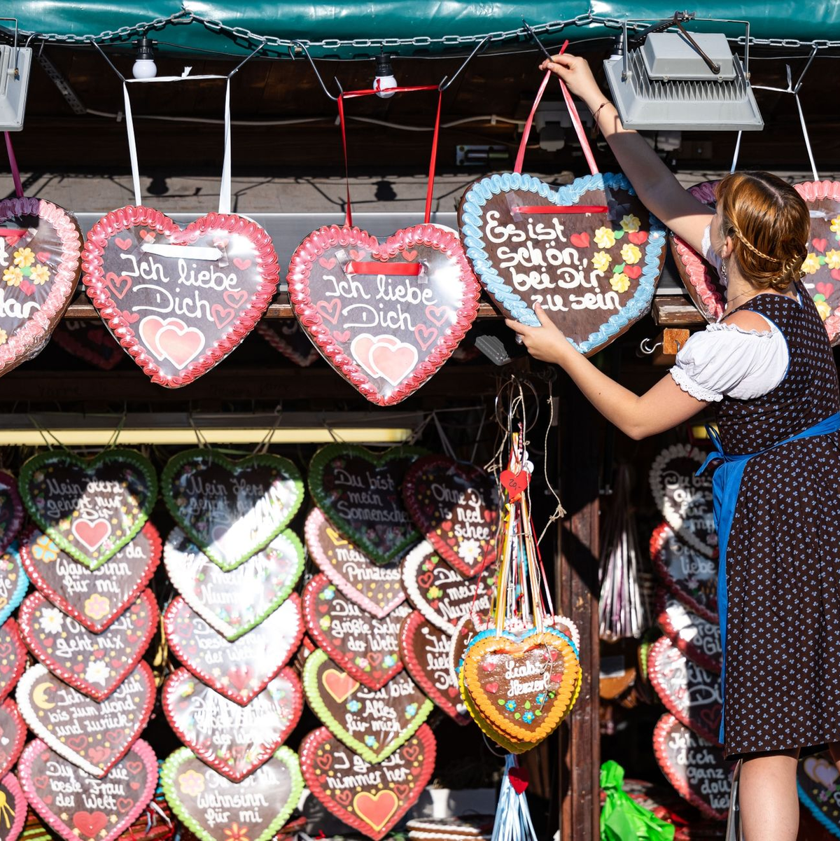 Eine Schaustellerin hängt ein Lebkuchenherz auf. - Foto: Lukas Barth/dpa