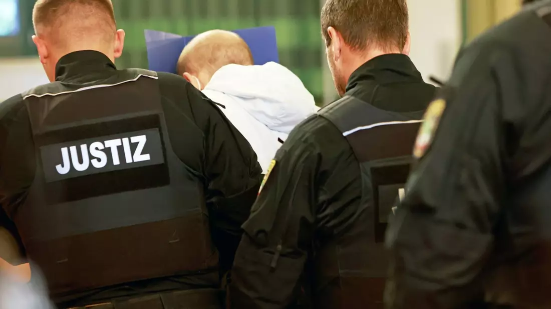 Der wegen Mordes angeklagte Mann (M) versteckt auf dem Weg in den Gerichtssaal sein Gesicht. - Bild: Matthias Bein/dpa