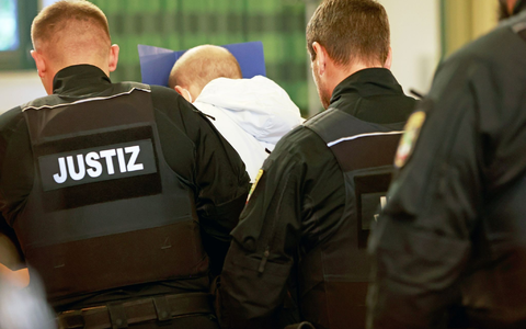 Der wegen Mordes angeklagte Mann (M) versteckt auf dem Weg in den Gerichtssaal sein Gesicht. - Foto: Matthias Bein/dpa