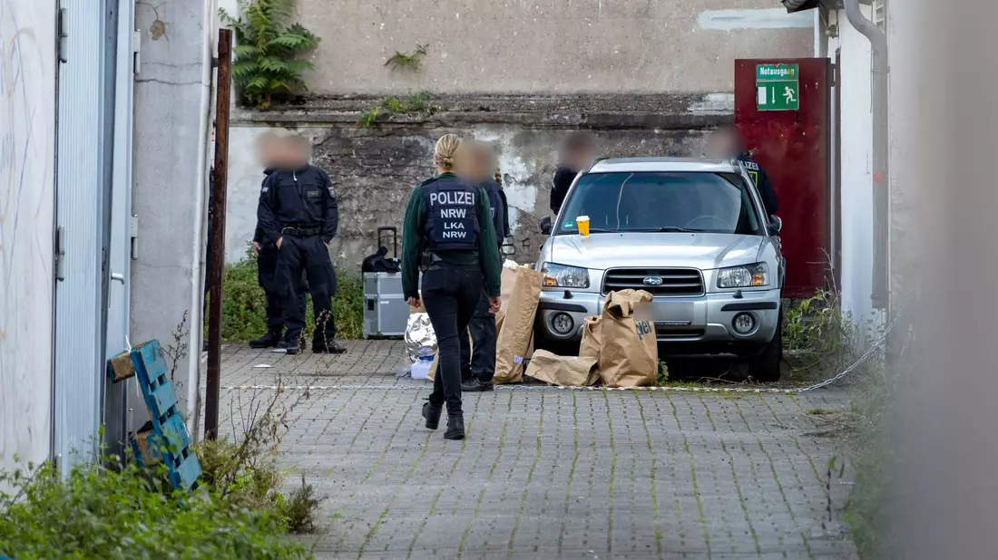 Polizistinnen und Polizisten stehen in einem Hinterhof in der Duisburger Innenstadt, auf dem Boden stehen Papiertüten mit Beweismitteln. - Bild: Christoph Reichwein/dpa