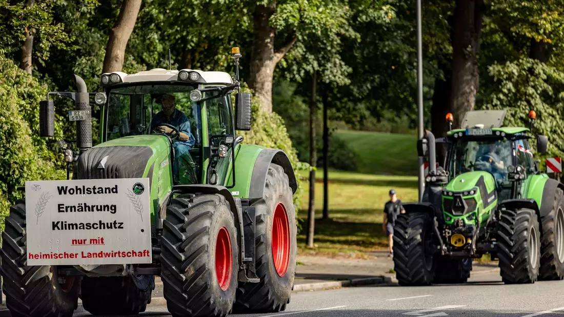Ein Traktor mit einem Plakat mit der Aufschrift «Wohlstand Ernährung Klimaschutz nur mit heimischer Landwirtschaft» fährt zum Auftakt der Agrarministerkonferenz durch die Kieler Innenstadt. - Bild: Axel Heimken/dpa