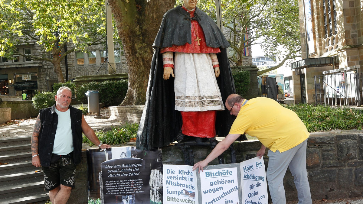 Nach Missbrauchsvorwürfen gegen den 1991 gestorbenen Essener Kardinal Hengsbach stellen die Betroffenenvertreter Markus Elstner (l) und Wilfried Fesselmann Protesttafeln auf. - Foto: Roland Weihrauch/dpa