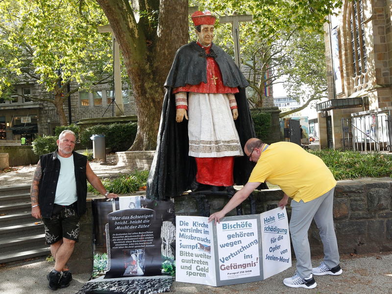 Nach Missbrauchsvorwürfen gegen den 1991 gestorbenen Essener Kardinal Hengsbach stellen die Betroffenenvertreter Markus Elstner (l) und Wilfried Fesselmann Protesttafeln auf. - Foto: Roland Weihrauch/dpa