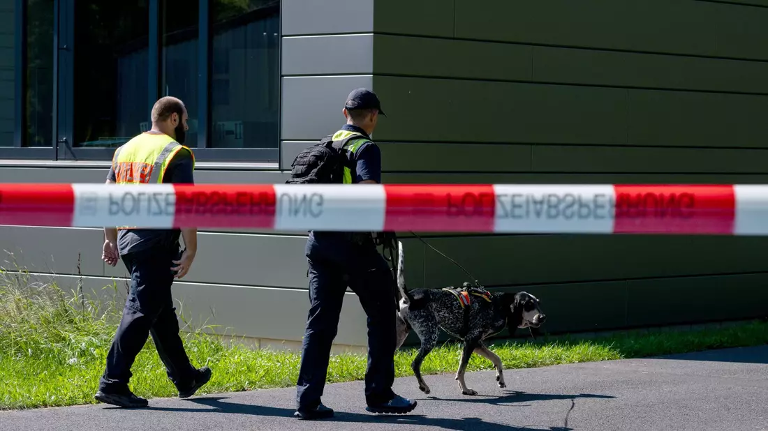 Polizeibeamte ermitteln mit einem Spürhund am Schulzentrum in Lohr am Main, wo der tote 14-Jährige gefunden wurde. - Bild: Pia Bayer/dpa