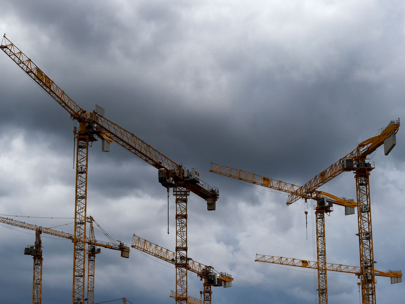 Dunkle Wolken ziehen über die Kräne auf einer Baustelle. «Alle Indikatoren am Bau zeigen deutlich nach unten, eine Trendwende ist nicht in Sicht», stellt die Bauindustrie fest. - Foto: Lisa Ducret/dpa
