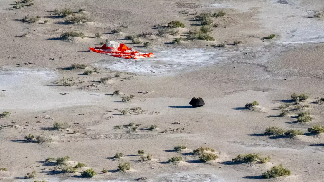 Die von der Raumsonde «Osiris-Rex» freigesetzte Kapsel liegt nach der Landung auf der Erde in der Nähe des Fallschirms. - Bild: Keegan Barber/NASA TV/AP/dpa