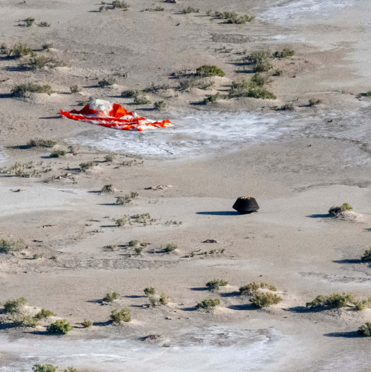 Die von der Raumsonde «Osiris-Rex» freigesetzte Kapsel liegt nach der Landung auf der Erde in der Nähe des Fallschirms. - Foto: Keegan Barber/NASA TV/AP/dpa