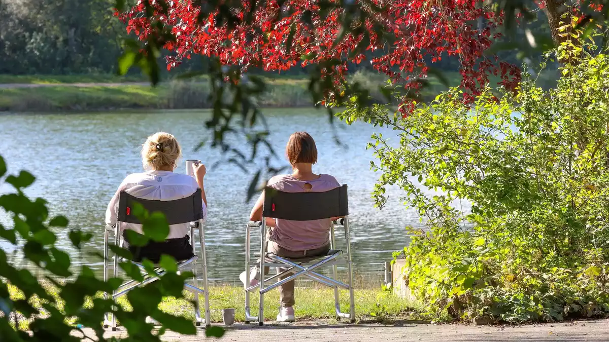 Zwei Frauen sitzen im baden-württembergischen Ertingen an einem See in der Sonne. - Bild: Thomas Warnack/dpa