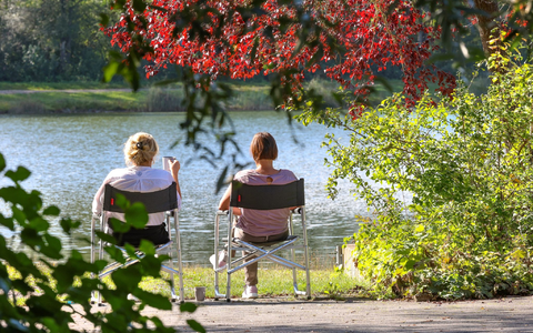 Zwei Frauen sitzen im baden-württembergischen Ertingen an einem See in der Sonne. - Foto: Thomas Warnack/dpa