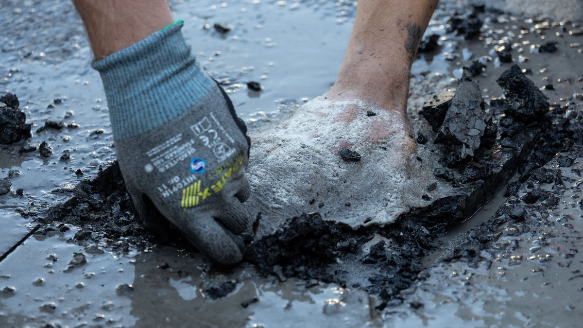 Ein Polizist entfernt Asphalt, um einen Aktivisten von der Straße zu lösen. - Foto: Hannes P. Albert/dpa