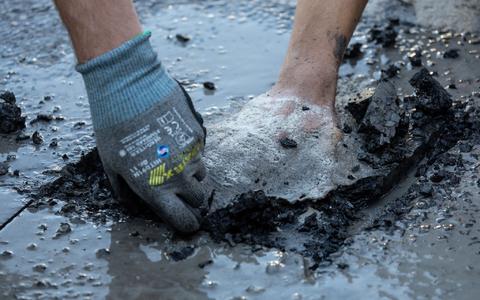 Ein Polizist entfernt Asphalt, um einen Aktivisten von der Straße zu lösen. - Foto: Hannes P. Albert/dpa