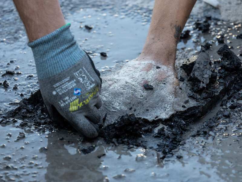 Ein Polizist entfernt Asphalt, um einen Aktivisten von der Straße zu lösen. - Foto: Hannes P. Albert/dpa