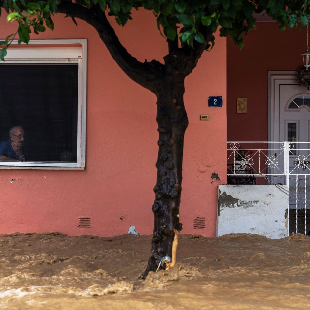 Ein Anwohner blickt aus dem Fenster seines Hauses auf die überschwemmte Straße. - Foto: Petros Giannakouris/AP/dpa