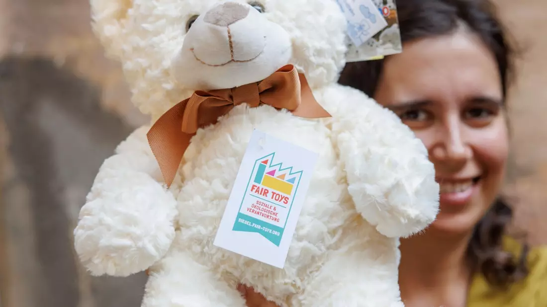 Eine Mitarbeiterin des Plüschtierherstellers Heunec präsentiert einen Stoffteddy, der mit dem Siegel der Fair Toys Organisation gekennzeichnet ist. - Bild: Daniel Karmann/dpa