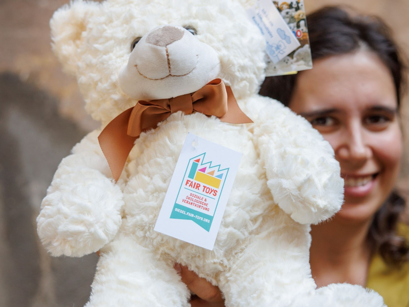 Eine Mitarbeiterin des Plüschtierherstellers Heunec präsentiert einen Stoffteddy, der mit dem Siegel der Fair Toys Organisation gekennzeichnet ist. - Foto: Daniel Karmann/dpa