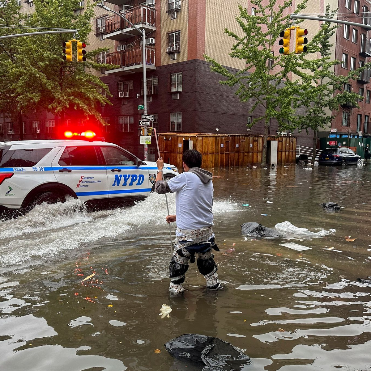 Hochwasser auf den Straßen von New York: Im Stadtteil Brooklyn versucht ein Mann, mit einem  Stock einen Abfluss zu reinigen, während ein Polizeiwagen vorbeifährt. - Foto: Jake Offenhartz/AP/dpa