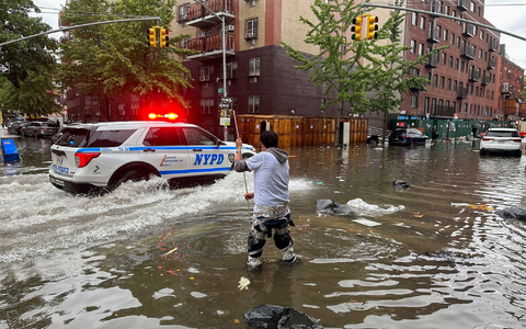 Hochwasser auf den Straßen von New York: Im Stadtteil Brooklyn versucht ein Mann, mit einem  Stock einen Abfluss zu reinigen, während ein Polizeiwagen vorbeifährt. - Foto: Jake Offenhartz/AP/dpa