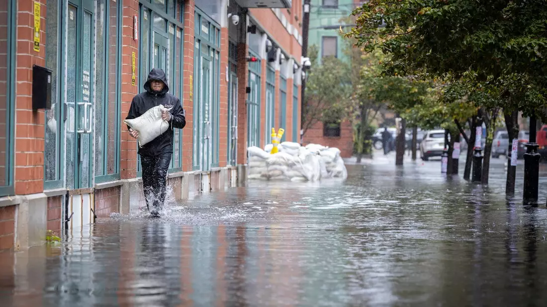 Mit Sandsäcken versucht ein Mann zu verhindern, dass Wasser in ein Gebäude eindringt. - Bild: Stefan Jeremiah/AP/dpa