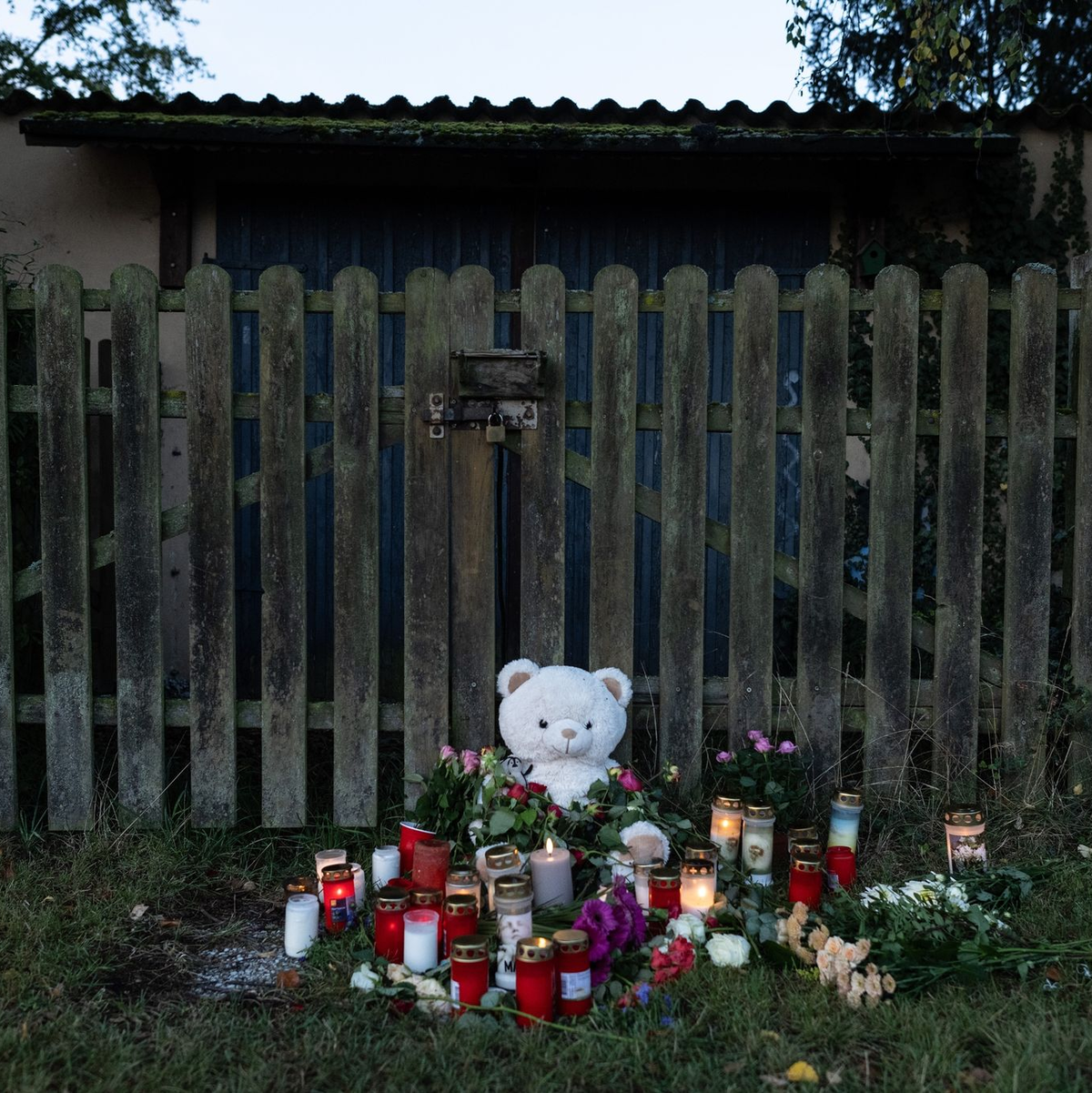 Kerzen, Blumen und ein großer Plüschteddy vor einem Zaun am Fundort der Leiche einer 14-Jährigen. - Foto: Swen Pförtner/dpa