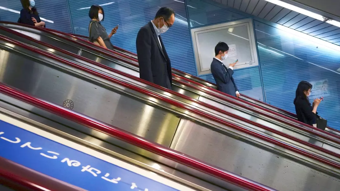 Menschen fahren auf einer Rolltreppe in eine U-Bahn-Station in Tokio. - Bild: Eugene Hoshiko/AP/dpa