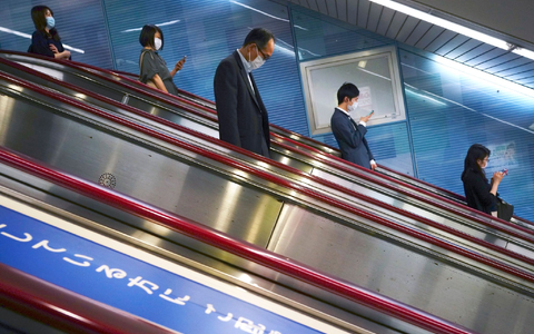 Menschen fahren auf einer Rolltreppe in eine U-Bahn-Station in Tokio. - Foto: Eugene Hoshiko/AP/dpa