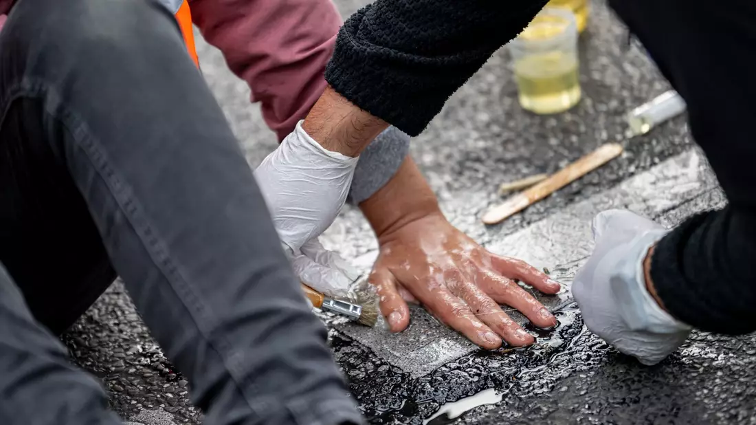 Eien Aktivistin der Letzten Generation hat sich auf die Straße geklebt. Ein Polizist versucht, ihre Hand vom Asphalt zu lösen. - Bild: Fabian Sommer/dpa