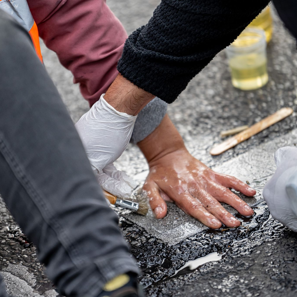 Eien Aktivistin der Letzten Generation hat sich auf die Straße geklebt. Ein Polizist versucht, ihre Hand vom Asphalt zu lösen. - Foto: Fabian Sommer/dpa