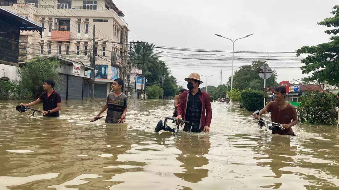 Anwohner schieben ihre Fahrräder durch eine überschwemmte Straße in Bago. - Bild: Thein Zaw/AP/dpa