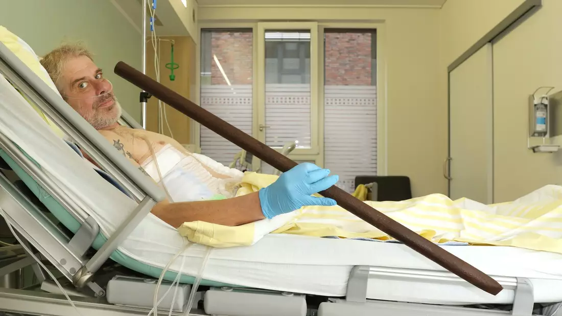 Patient Frank Vaorin liegt im Krankenhausbett und hält die Zaunstange in der Hand, die seinen Körper durchbohrte. - Bild: Kerstin Hase/Gesundheit Nord – Klinikverbund Bremen/dpa
