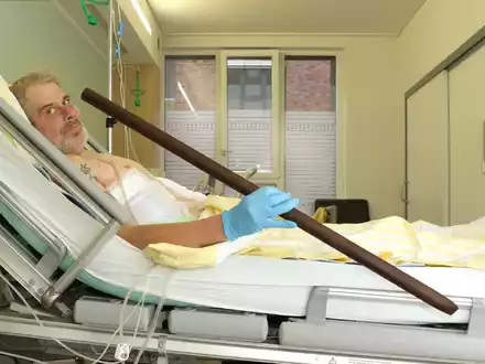 Patient Frank Vaorin liegt im Krankenhausbett und hält die Zaunstange in der Hand, die seinen Körper durchbohrte. - Foto: Kerstin Hase/Gesundheit Nord – Klinikverbund Bremen/dpa