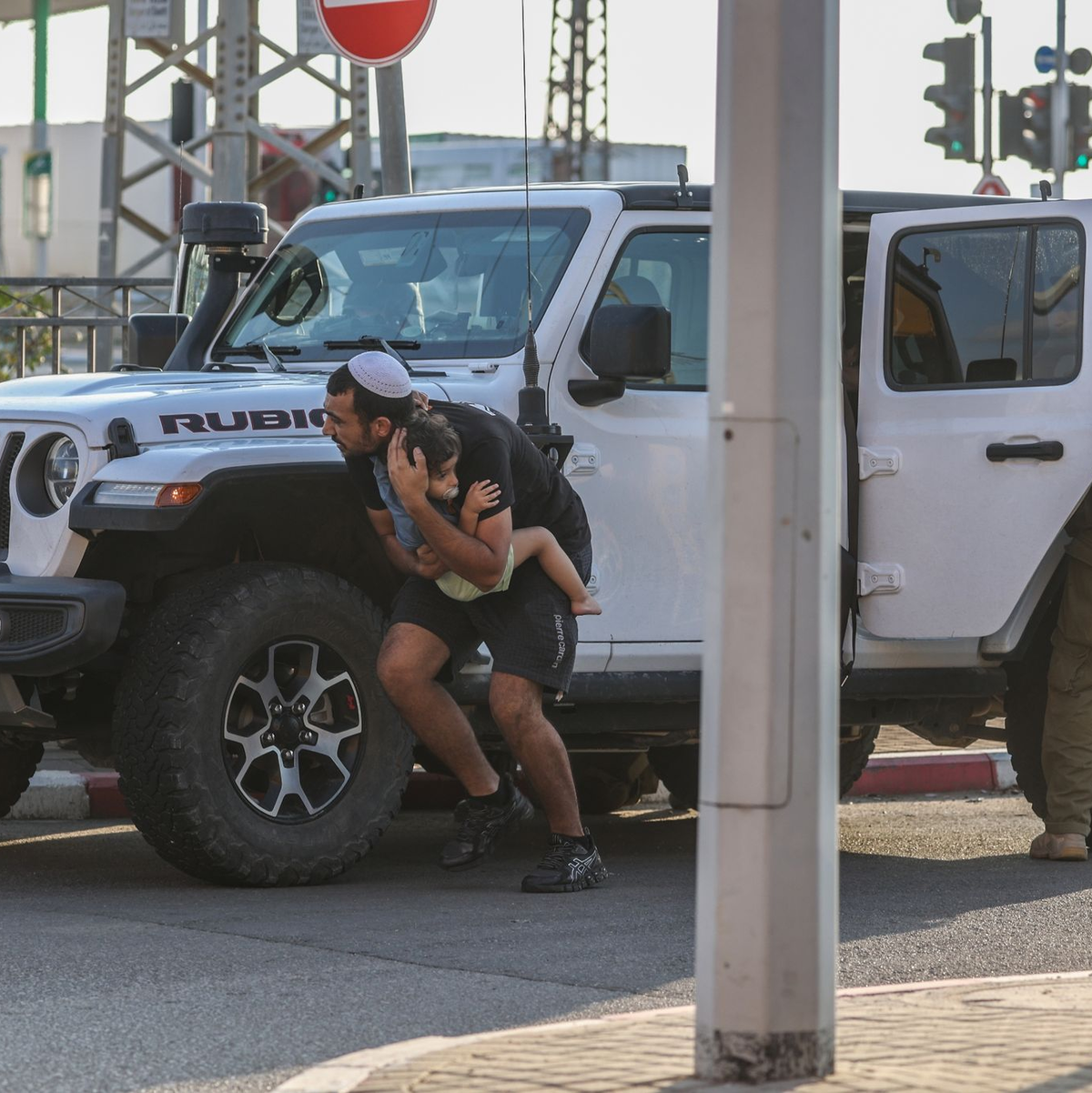 Ein Mann hält in Ashkelon ein Kind im Arm und sucht bei einem neuen Raketenangriff aus Gaza hinter einem Fahrzeug Deckung. - Foto: Ilia yefimovich/dpa