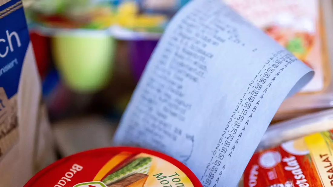 Ein Kassenbon im Einkaufskorb: Die Menschen in Deutschland fürchten sich einer Umfrage zufolge vor steigenden Lebenshaltungskosten. - Bild: Monika Skolimowska/dpa