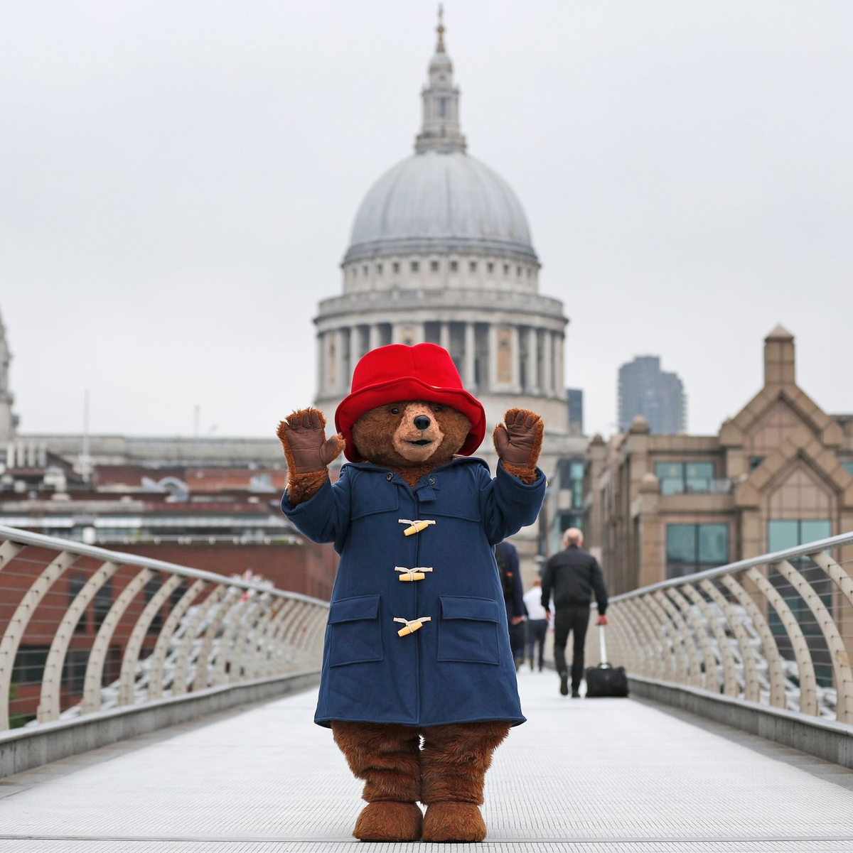Ein Darsteller im Kostüm des Paddington-Bär  auf der Millenium-Brücke vor der Kuppel der St.-Pauls-Kathedrale in London. - Foto: Frank Augstein/AP/dpa