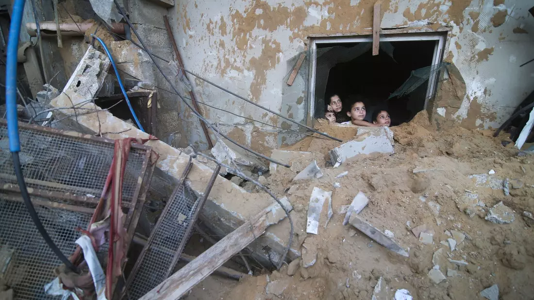 Palästinensische Kinder schauen in Rafah im Süden des Gazastreifens aus einem Fenster, das bei israelischen Luftangriffen zerstört wurde. - Bild: Hatem Ali/AP/dpa