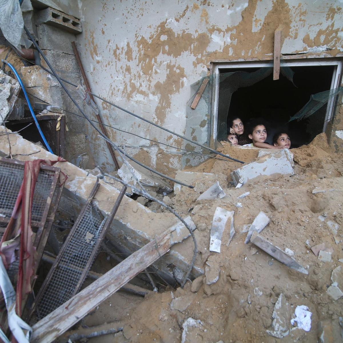 Palästinensische Kinder schauen in Rafah im Süden des Gazastreifens aus einem Fenster, das bei israelischen Luftangriffen zerstört wurde. - Foto: Hatem Ali/AP/dpa