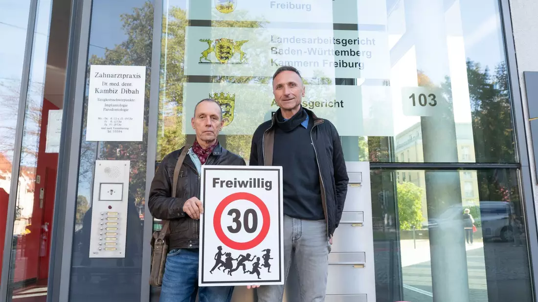 Christian Kronbitter (l) und Erich Maier vor dem Verwaltungsgericht in Freiburg mit einem «Freiwillig 30»-Schild. - Bild: Silas Stein/dpa