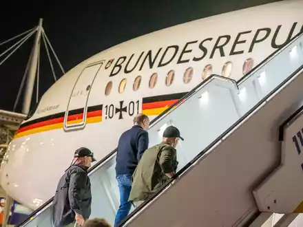 Bodyguards bringen Bundeskanzler Olaf Scholz nach dem Luftalarm in den Regierungs-Airbus. - Foto: Michael Kappeler/dpa Pool/dpa