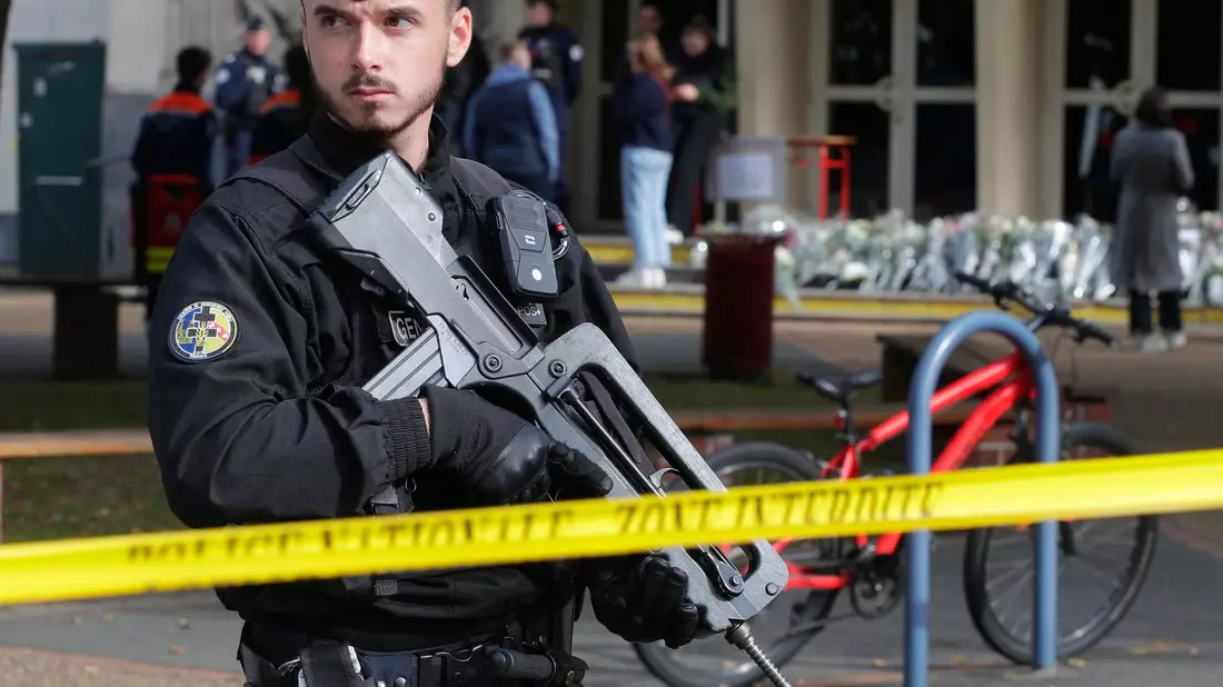 Ein schwer bewaffneter französischer Polizist vor einem Gymnasium (Archivbild). In Frankreich häufen sich seit einigen Tagen Bombendrohungen, insbesondere gegen Schulen - nun gibt es auch welche gegen mehrere Regionalflughäfen. - Bild: Michel Spingler/AP/dpa