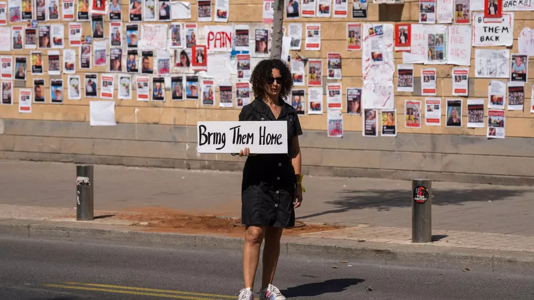 «Bringt sie nacht Hause» steht auf dem Schild dieser Frau, die in Tel Aviv vor einer Wand mit den Fotos von Israelis steht, die von der Hamas im Gazastreifen gefangen gehalten werden. - Bild: Petros Giannakouris/AP/dpa