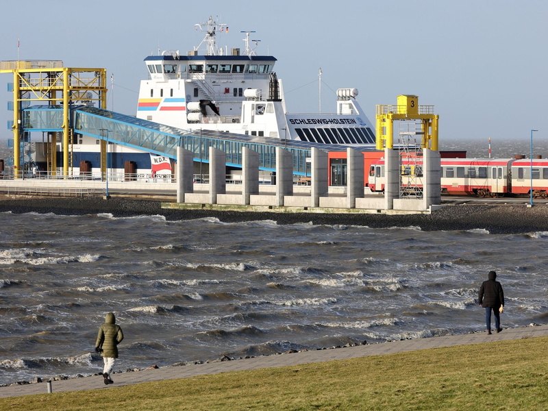 Spaziergänger sind bei stürmischem Wetter am Hafen von Dagebüll unterwegs. (Archivbild) - Foto: Bodo Marks/dpa