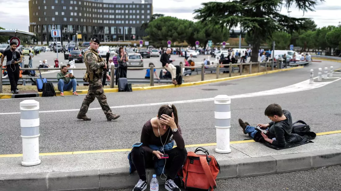 Reisende warten, während ein französischer Soldat vor dem Flughafen Toulouse-Blagnac patrouilliert. - Bild: Charly Triballeau/AFP/dpa