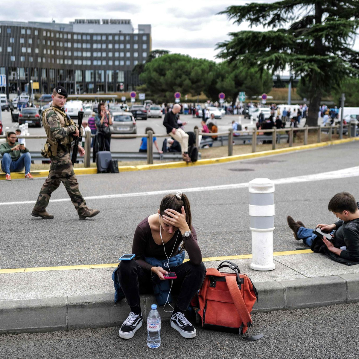 Reisende warten, während ein französischer Soldat vor dem Flughafen Toulouse-Blagnac patrouilliert. - Foto: Charly Triballeau/AFP/dpa