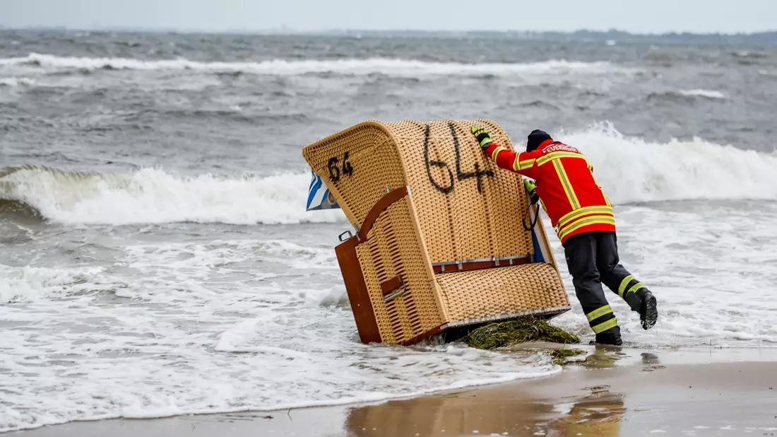 Ein Feuerwehrmann versucht, in Kiel-Schiksee einen Strandkorb vor den Flutwellen der Ostsee zu sichern. - Bild: Axel Heimken/dpa