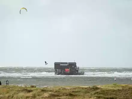 Ein Kiter fliegt über das Wasser auf dem überfluteten Strand in St. Peter Ording - Foto: Jonas Walzberg/dpa