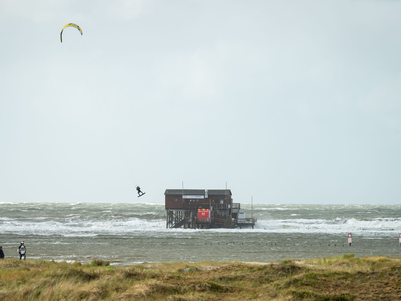 Ein Kiter fliegt über das Wasser auf dem überfluteten Strand in St. Peter Ording - Foto: Jonas Walzberg/dpa