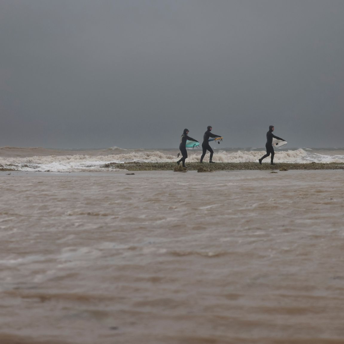 Surfer gehen über den überfluteten Ostseestrand in Eckernförde zum Meer. - Foto: Frank Molter/dpa