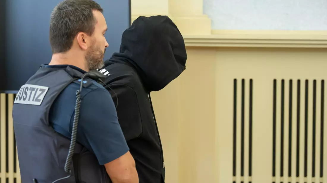 Der Angeklagte (r) wird vor Prozessbeginn in den Gerichtssaal gebracht. Gegen ihn wurde eine lebenlange Haftstrafe verhängt. - Bild: Silas Stein/dpa
