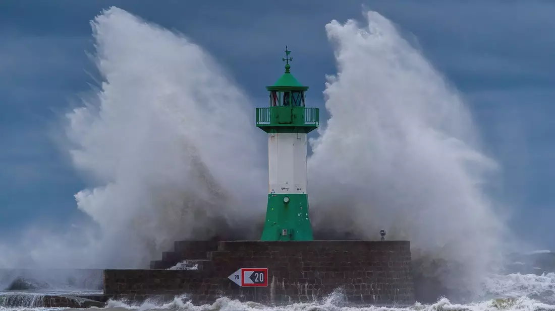 Wellen der Ostsee peitschen bei einem schweren Sturmtief an den Leuchtturm auf der Ostmole. Wegen des Sturmtiefs sind an der Ostseeküste Straßen und Uferbereiche vom Hochwasser überschwemmt worden. - Bild: Georg Moritz/dpa