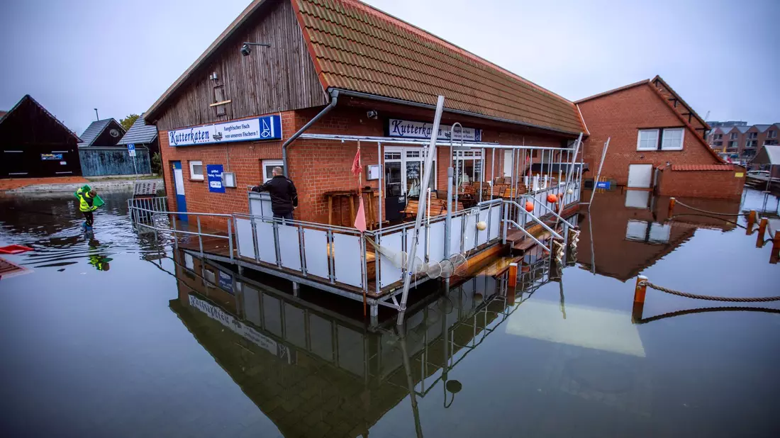 Fahrräder stehen an einer überfluteten Straßenkreuzung in der Nähe des Fischereihafens in Wismar im Wasser. - Bild: Jens Büttner/dpa